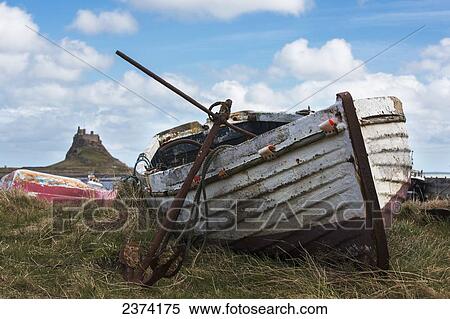Stock Photography - An old boat and rusted anchor abandoned on the shore with Lindisfarne Castle in the background; Holy Island, Northumberland, England. Fotosearch