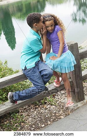 Stock Photo - Brother and sister in a park whispering in each other's ears; Menlo Park, California, United States of America. Fotosearch