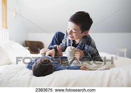Stock Photography - Brothers playing on a big bed at home; Victoria, British Columbia, Canada. Fotosearch