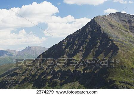 Stock Photo - Close up of eroded mountain side with blue sky and clouds; Yukon, Canada. Fotosearch