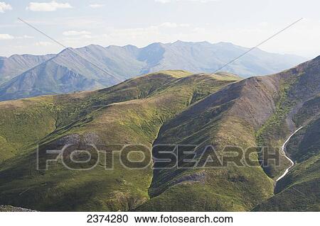 Stock Image - Close up of rolling mountain hillside with mountain range in the background; Yukon, Canada. Fotosearch