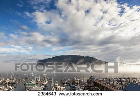 Stock Image - Clouds and fog form over Mount Tzouhalem and above the seaside village of Cowichan Bay; British Columbia, Canada. Fotosearch