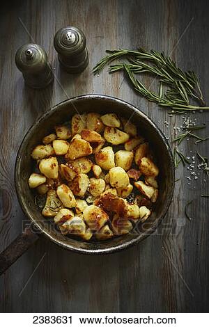 Stock Image - Crunchy potatoes with rosemary in an old iron pan. Fotosearch
