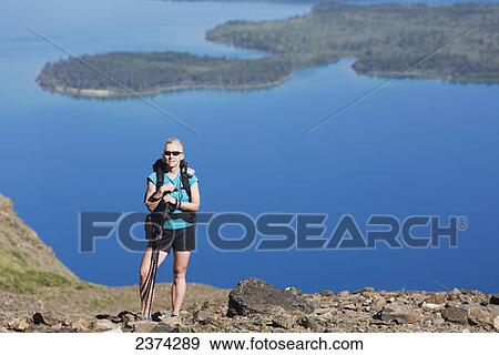 Female hiker standing on mountain rocky trail with mountain lake below in the background; Yukon, Canada View Large Photo Image Stock Photo - Female hiker standing on mountain rocky trail with mountain lake below in the background; Yukon, Canada. Fotosearch