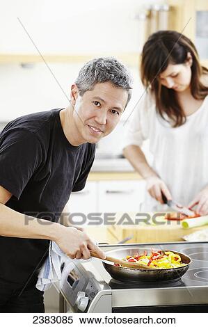 Stock Photography - Husband and wife cooking together in the kitchen; Montreal, Quebec, Canada. Fotosearch