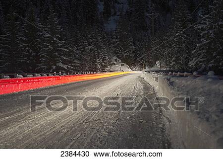 Stock Image - Light trail from a vehicle taillight on a snowy road at nighttime; Ticino, Switzerland. Fotosearch