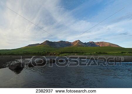 Stock Photo - Looking across a small river to the peaks and ridges of the Black Cuillin at sunset; Isle of Skye, Scotland. Fotosearch