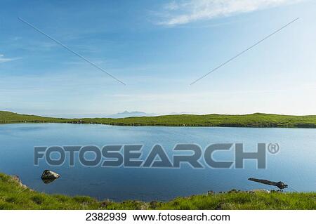 Stock Photo - Looking across small, calm lake over to the Isle of Rum in the distance; Isle of Skye, Scotland. Fotosearch