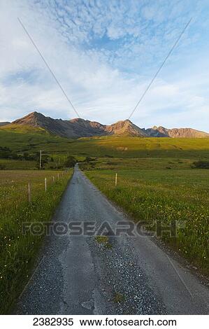 Stock Photography - Looking up a road towards the peaks and ridges of the Black Cuillin at sunset; Isle of Skye, Scotland. Fotosearch