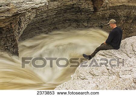 Stock Image - Man watches the Trout River flowing over Whittaker Falls along the Mackenzie Highway; Northwest Territories, Canada. Fotosearch