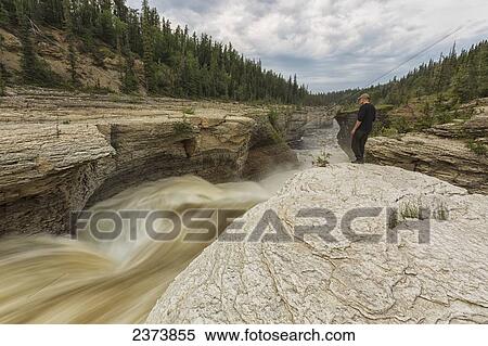 Man watches the Trout River flowing over Whittaker Falls along the Mackenzie Highway; Northwest Territories, Canada View Large Photo Image Stock Photography - Man watches the Trout River flowing over Whittaker Falls along the Mackenzie Highway; Northwest Territories, Canada. Fotosearch