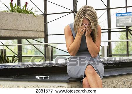 Stock Photo - Mature Professional Businesswoman In Downtown Office Environment Holding Her Face In Her Hands; Edmonton, Alberta, Canada. Fotosearch