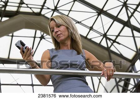 Stock Photograph - Mature Professional Businesswoman In Downtown Office Environment Using Cell Phone; Edmonton, Alberta, Canada. Fotosearch