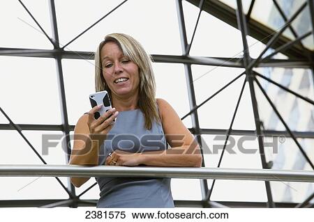 Stock Photography - Mature Professional Businesswoman In Downtown Office Environment Using Cell Phone; Edmonton, Alberta, Canada. Fotosearch