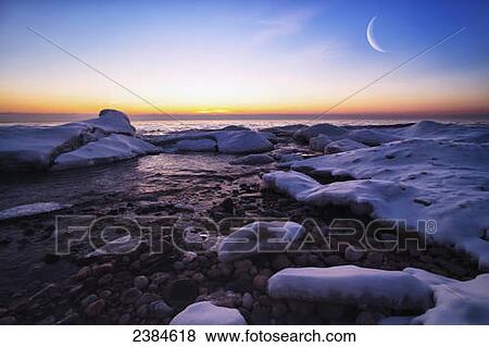 Stock Photo - On the icy shores of Lake Michigan the moon (double exposed) and ice creates a beautiful morning; Wisconsin, United States of America. Fotosearch