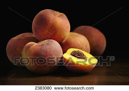 Stock Image - Peaches sitting on a wooden table, one cut in half; Montreal, Quebec, Canada. Fotosearch