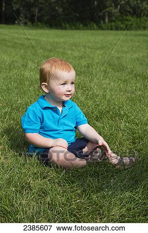Stock Photo - Portrait of a baby with red hair sitting in the grass; Stony Plain, Alberta, Canada. Fotosearch