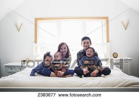 Stock Photo - Portrait of five siblings on a bed; Victoria, British Columbia, Canada. Fotosearch
