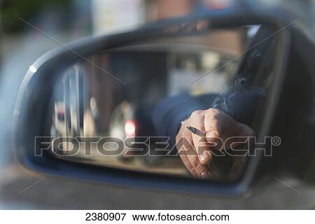 Reflection in the mirror of a vehicle of a hand holding a cigarette; Locarno, Ticino, Switzerland View Large Photo Image Stock Photo - Reflection in the mirror of a vehicle of a hand holding a cigarette; Locarno, Ticino, Switzerland. Fotosearch