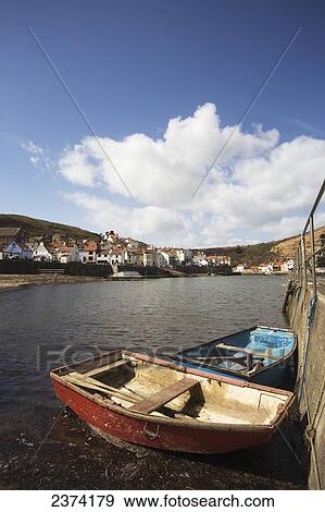 Stock Photo - Rowboats tied along the shore with houses along the waterfront; Staithes, Yorkshire, England. Fotosearch