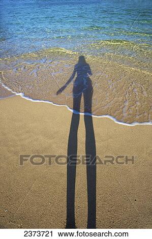 Shadow of a woman standing on the beach at the water's edge; Kauai, Hawaii, United States of America View Large Photo Image Stock Image - Shadow of a woman standing on the beach at the water's edge; Kauai, Hawaii, United States of America. Fotosearch