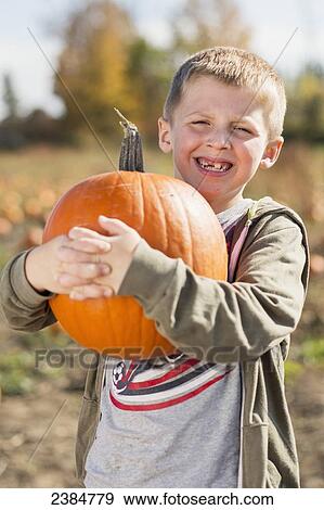 Stock Photo - Smiling gap toothed boy with pumpkin in a pumpkin patch; Trenton, Ontario, Canada. Fotosearch