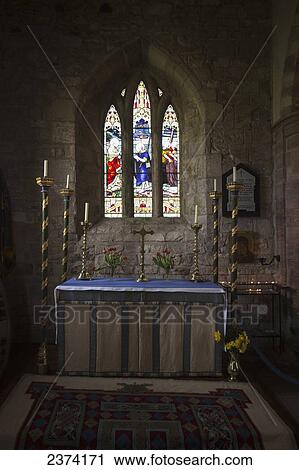 Stock Image - Stained glass windows and a table surrounded with candles in a church; Bamburgh, Northumberland, England. Fotosearch