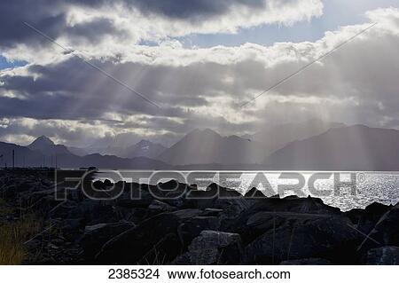 Picture - Sun rays through dramatic clouds over the water; Homer, Alaska, United States of America. Fotosearch
