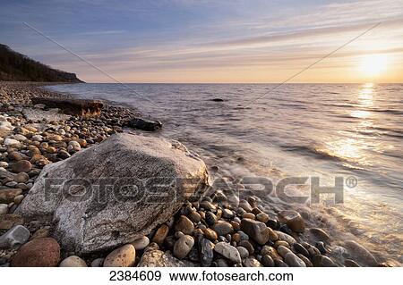 Stock Photo - Sunrise kisses rock and water as it rises on the shores of Lake Michigan; Wisconsin, United States of America. Fotosearch