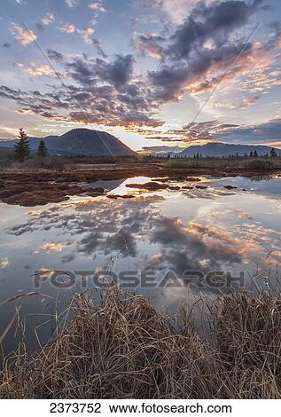 Stock Image - The sunset and goat mountain are being reflected into an unnamed pond along the Annie Lake Road, near Whitehorse; Yukon, Canada. Fotosearch