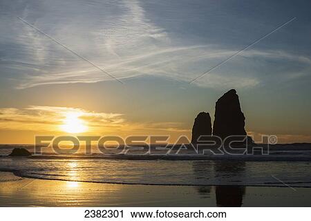 The sunset with silhouettes of rock formations reflected in the wet sand; Cannon Beach, Oregon, United States of America View Large Photo Image Stock Image - The sunset with silhouettes of rock formations reflected in the wet sand; Cannon Beach, Oregon, United States of America. Fotosearch