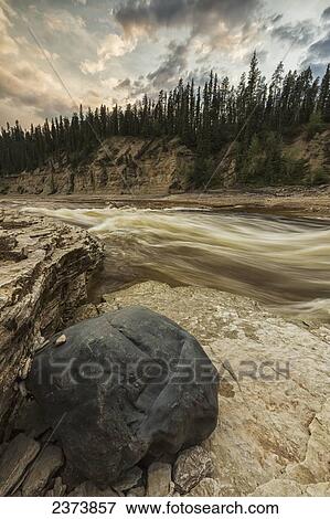 Stock Photo - The Trout River flows by a large rock as the day comes to an end, Sambaa Deh Territorial Park; Northwest Territories, Canada. Fotosearch