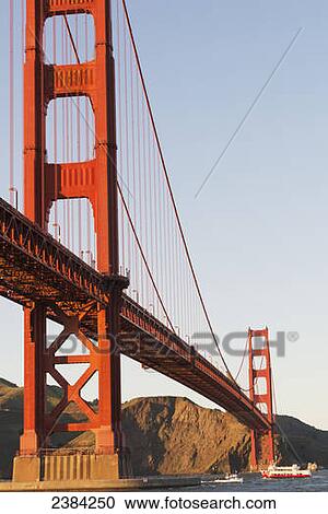 Stock Image - Tour boats cross under Golden Gate Bridge, viewed from Fort Point at the entrance to San Francisco Bay, Marin Headlands visible in background; San Francisco, California, United States of America. Fotosearch