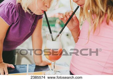 Picture - Two young girls share a drink with straws; Peachland, British Columbia, Canada. Fotosearch