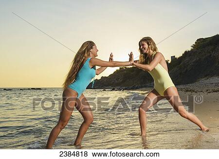 Stock Photo - Two young women in bathing suits playing on the beach at sunset; Tarifa, Cadiz, Andalusia, Spain. Fotosearch