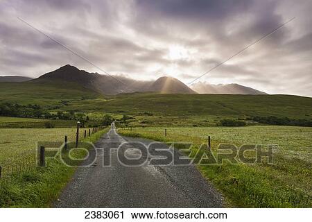 View along a road early in the morning with the rising sun behind the Black Cuillin Ridge; Glen Brittle, Skye, Scotland View Large Photo Image Stock Image - View along a road early in the morning with the rising sun behind the Black Cuillin Ridge; Glen Brittle, Skye, Scotland. Fotosearch