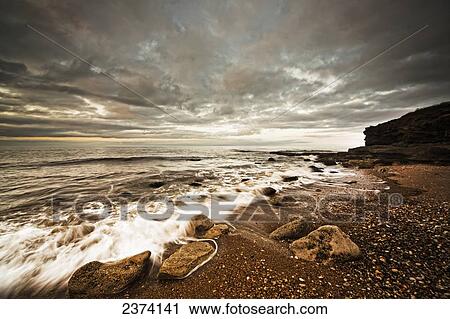 Water washing up on the shore along the coastline under a cloudy sky; Tyne and Wear, England View Large Photo Image Stock Image - Water washing up on the shore along the coastline under a cloudy sky; Tyne and Wear, England. Fotosearch