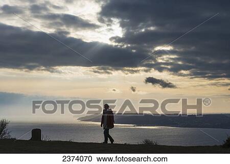 Woman walking near the top of Golden Cap with Lyme Regis behind, Jurassic Coast; Dorset, England View Large Photo Image Stock Image - Woman walking near the top of Golden Cap with Lyme Regis behind, Jurassic Coast; Dorset, England. Fotosearch