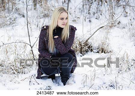 Stock Photo - A blonde female in winter fashion attire crouches in the snow; Fort McMurray, Alberta, Canada. Fotosearch