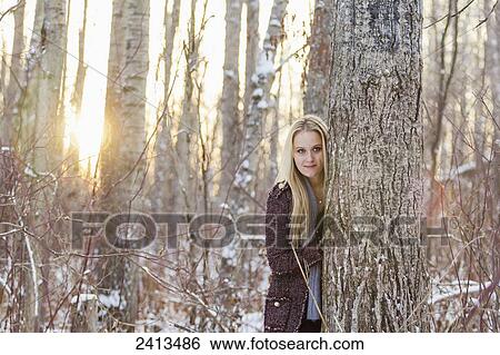 A blonde female in winter fashion attire looks out from behind a tree in the snow; Fort McMurray, Alberta, Canada View Large Photo Image Stock Photograph - A blonde female in winter fashion attire looks out from behind a tree in the snow; Fort McMurray, Alberta, Canada. Fotosearch