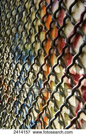 Stock Photo - A chain link fence against a wall with colourful spray painted graffiti; Barcelona, Spain. Fotosearch