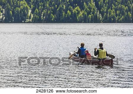 Stock Photograph - A couple and young girl in a red canoe on Byers lake with green forested shoreline in Byers Lake Campground, Denali State Park; Alaska, United States of America. Fotosearch
