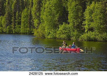 Stock Photography - A couple and young girl in a red canoe on Byers lake with green forested shoreline in Byers Lake Campground, Denali State Park; Alaska, United States of America. Fotosearch
