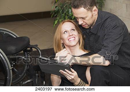 Stock Photo - A couple looking at a tablet together, wife with a disability; Edmonton, Alberta, Canada. Fotosearch