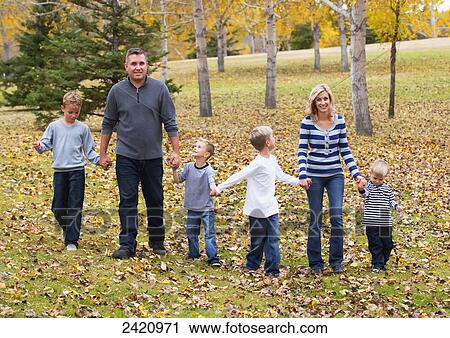 Stock Image - A family with four sons walking and holding hands in a park in autumn; Edmonton, Alberta, Canada. Fotosearch