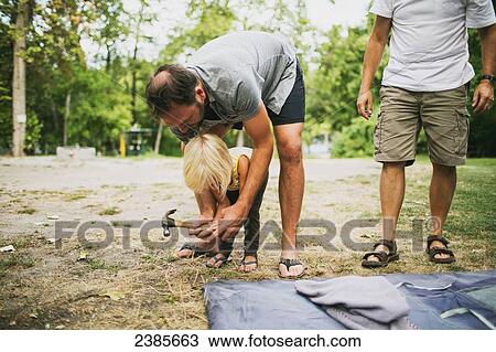 Stock Image - A father and young daughter work together to hammer in tent pegs at a campsite; Peachland, British Columbia, Canada. Fotosearch