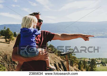 Picture - A father holds his young daughter as they look out over Lake Okanagan; Peachland, British Columbia, Canada. Fotosearch