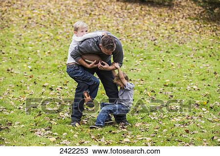 Stock Image - A father playing football with his boys in a park in autumn; Edmonton, Alberta, Canada. Fotosearch