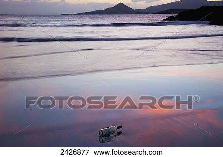 Stock Photo - A glass bottle lays on the wet sand at the water's edge at sunset; County Kerry, Ireland . Fotosearch