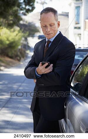 Stock Photo - A man in a suit by the car checking his cell phone; San Francisco, California, United States of America. Fotosearch